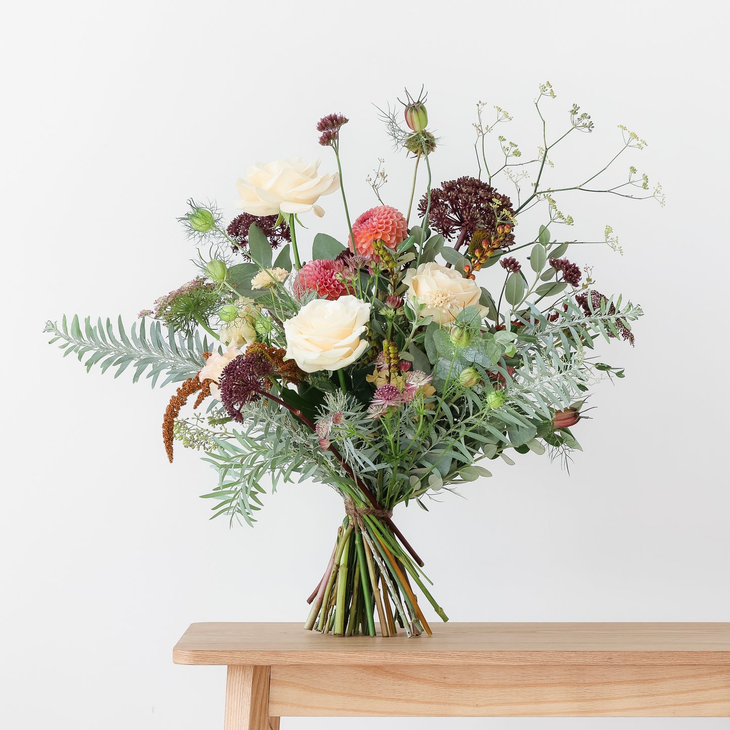 A Seasonal Bouquet with a variety of flowers including whites, pinks, and greens, arranged in a loose, natural style on a wooden table.
