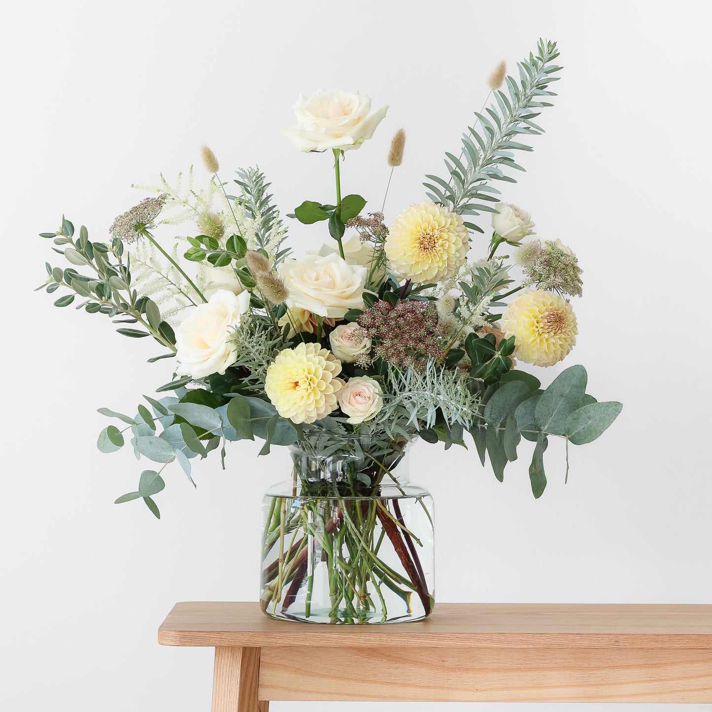 A clear glass vase filled with an arrangement of seasonal flowers including yellow and white blooms, and green foliage.