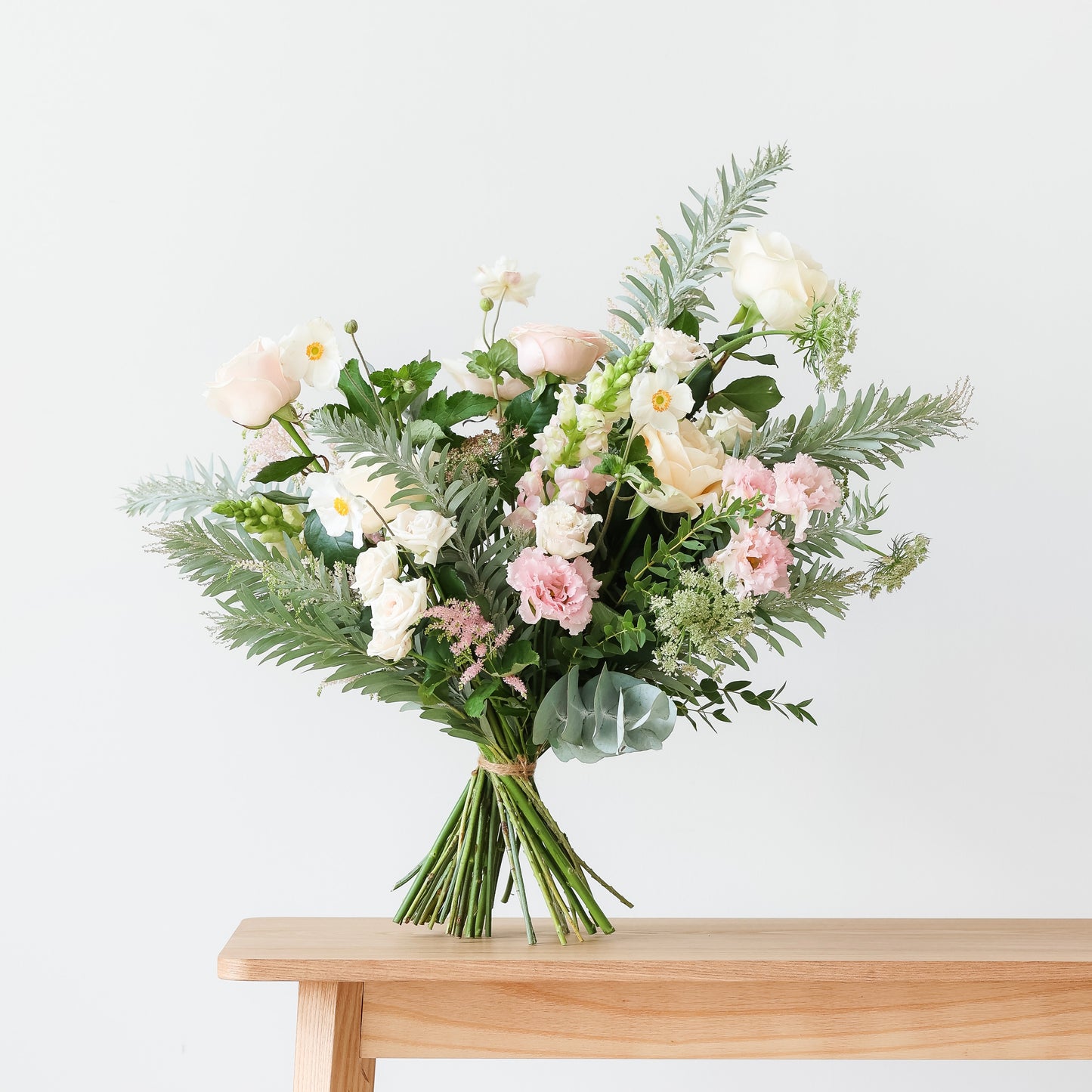 A handtied bouquet of white, soft pink and peach flowers and foliage.