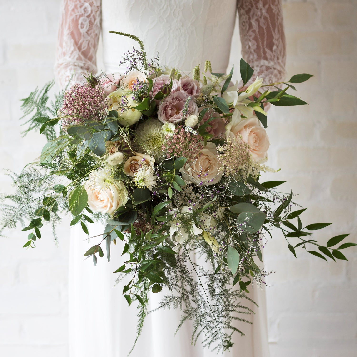 A handtied bridal bouquet with a mix of seasonal flowers in shades of pink, green, and white, bound with a satin ribbon.