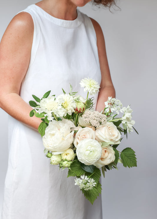 Person holding a bridesmaid bouquet of white and green flowers against a plain background