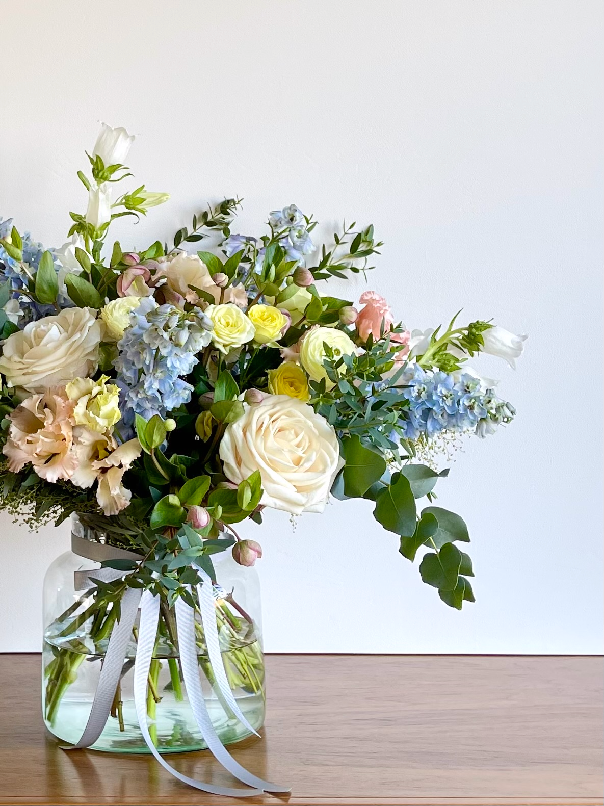A Mother's Daybouquet of pastel coloured flowers in a glass vase with white ribbon
