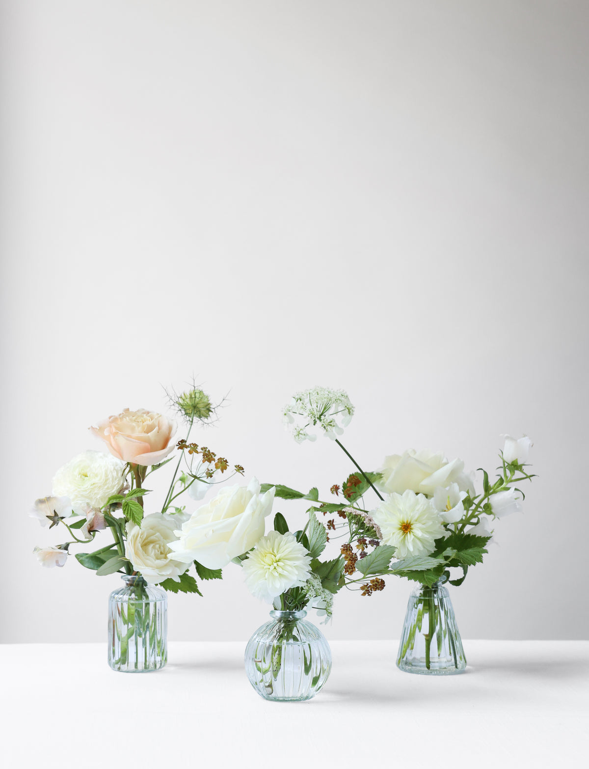 A trio of perfume bottles with wedding flowers on a white table